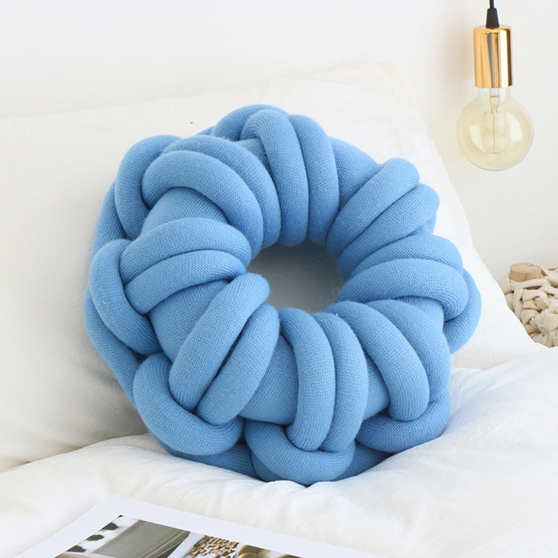 blue donut knotte cushion on a white bed