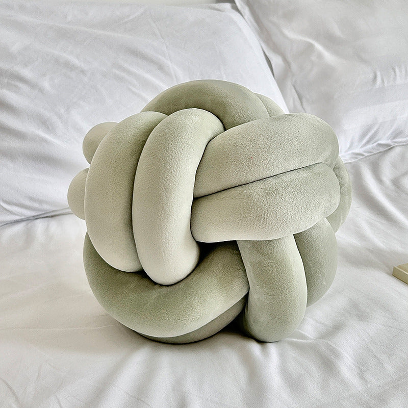 light green knot pillow on a white bed