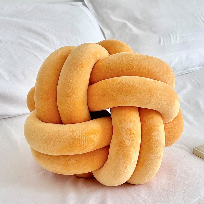 orange knot pillow on a white bed