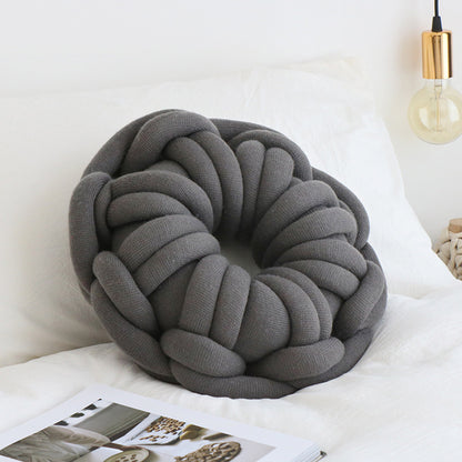 dark grey donut knotte cushion on a white bed