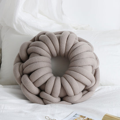 light grey donut knotte cushion on a white bed