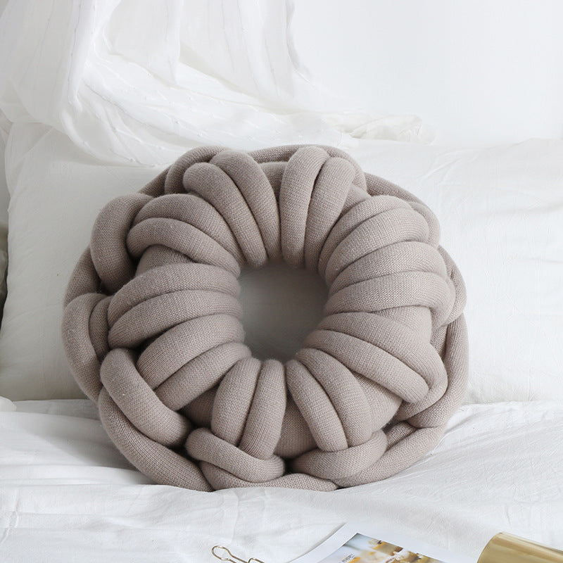 light grey donut knotte cushion on a white bed