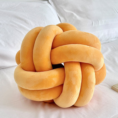 orange knot pillow on a white bed